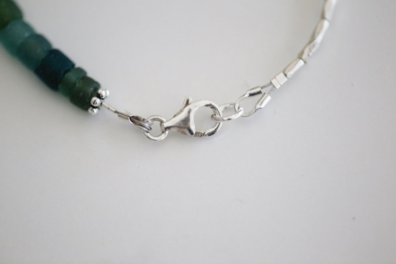 Detailed view of a silver clasp on a green beaded bracelet against a white background.